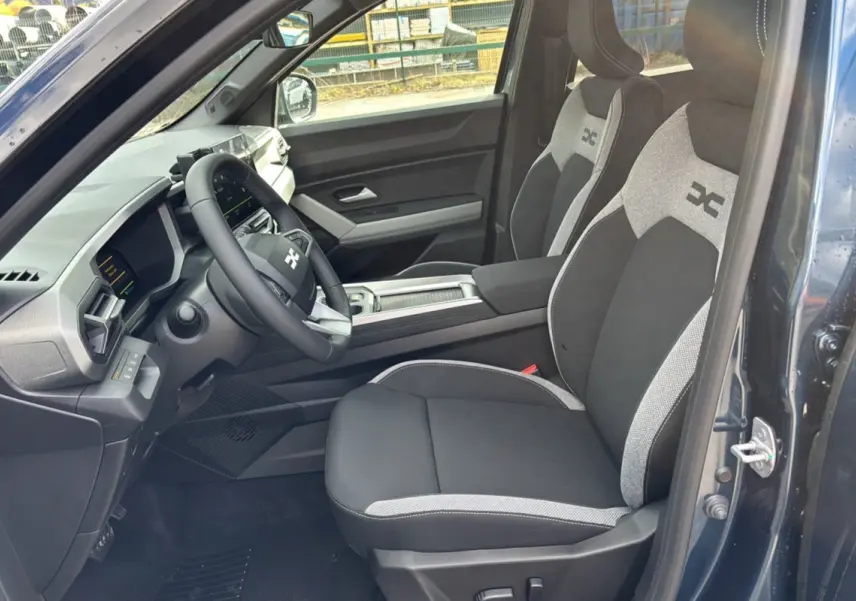 Vue intérieure côté conducteur du Dacia Bigster Hybrid 155 Journey Plus 2026 bleu indigo, sièges tissu noir et gris avec logo.