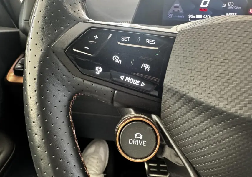 Gros plan sur le volant cuir perforé noir du Cupra Born 230ch avec commandes multifonctions et bouton Drive.