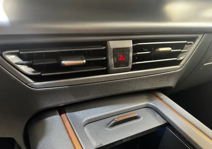 Gros plan sur la console centrale intérieure grise du CUPRA BORN 230ch, avec aérateurs et bouton de signalisation d'urgence rouge.
