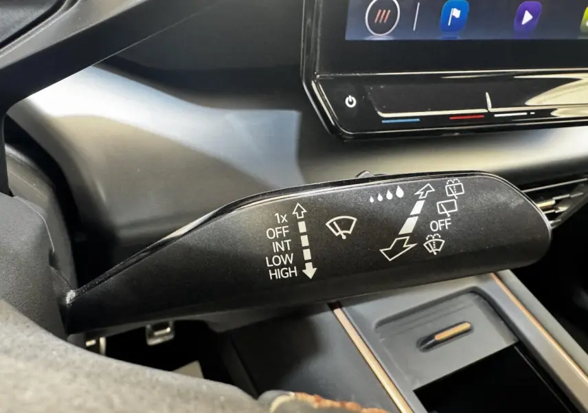 Gros plan sur la commande des essuie-glaces dans l’habitacle sombre d’une CUPRA BORN gris foncé, écran tactile en arrière-plan.