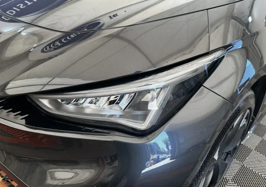 Gros plan sur le phare avant droit du CUPRA BORN gris foncé 2023 avec détails LED et carrosserie brillante.