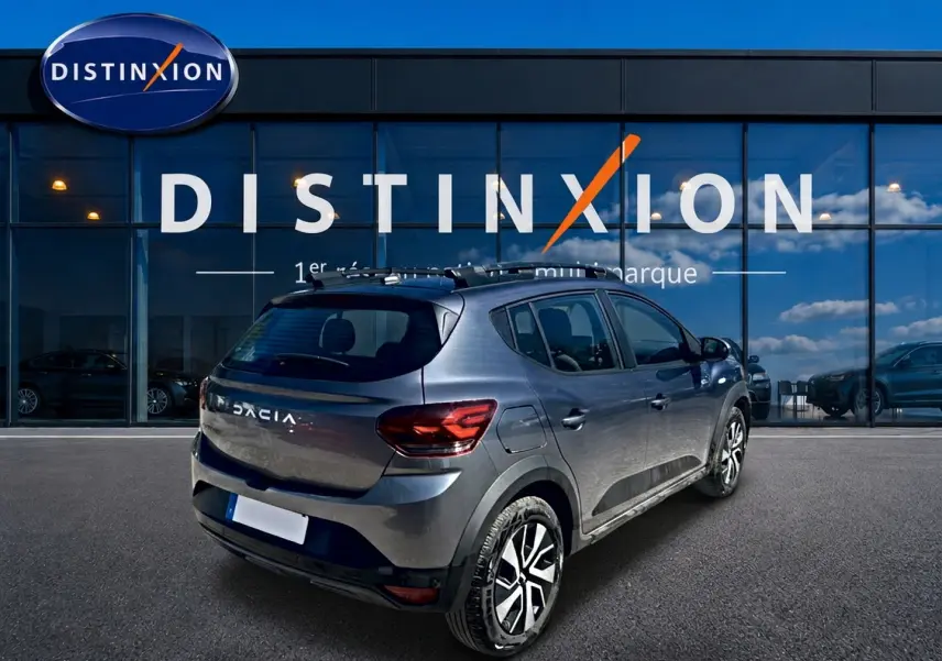 Vue 3/4 arrière droite d'une Dacia Sandero Stepway gris schiste avec barres de toit et jantes alliage noires.