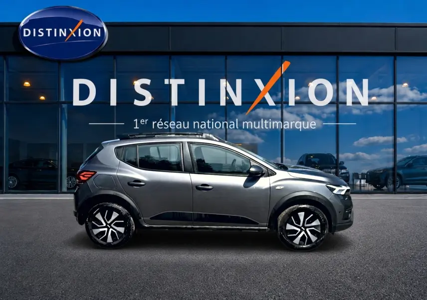 Profil droit d'une Dacia Sandero Stepway gris schiste 2025 avec barres de toit et jantes noires stylisées.