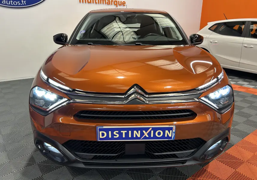 Citroën C4 PureTech 100 Feel orange vue de face avec phares allumés et attelage visible sous le pare-chocs.