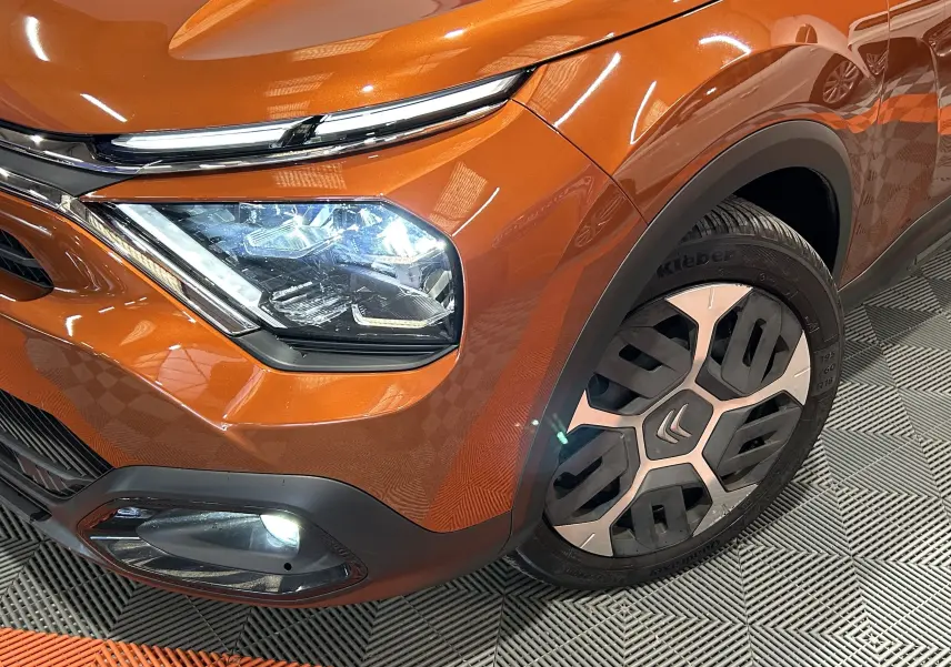 Gros plan sur l'avant droit orange vif d'une Citroën C4 PureTech 100 Feel avec phares allumés et jante distinctive.