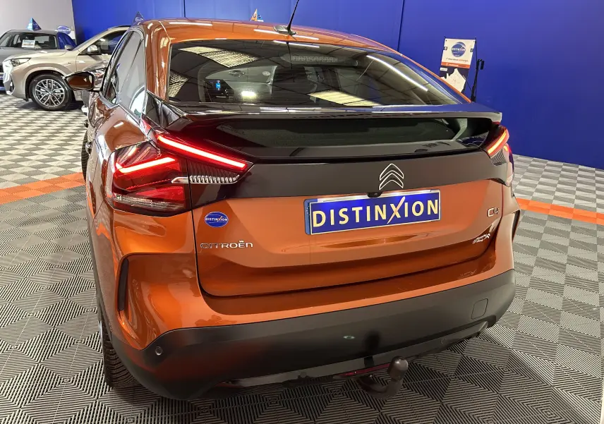 Vue 3/4 arrière droite d'une Citroën C4 orange 2021 avec attelage et caméra de recul en intérieur showroom.