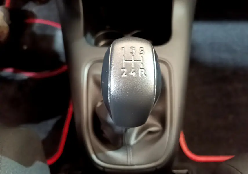 Le levier de vitesses manuel gris de la Citroën C3 PureTech 68 BVM Live vu de dessus, entouré de tapis noirs avec surpiqûres rouges.