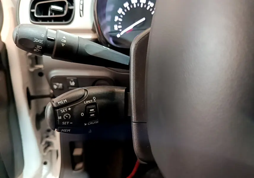 Gros plan sur les commandes de régulateur de vitesse et feux au volant d'une Citroën C3 blanche de 2018.