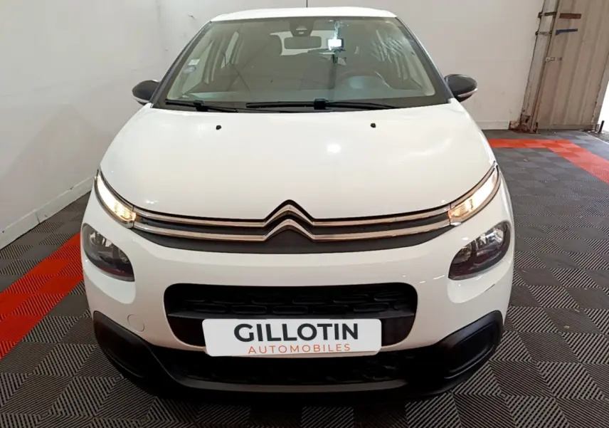 Vue frontale d'une Citroën C3 blanche de 2018 avec phares allumés et calandre distinctive en intérieur showroom.