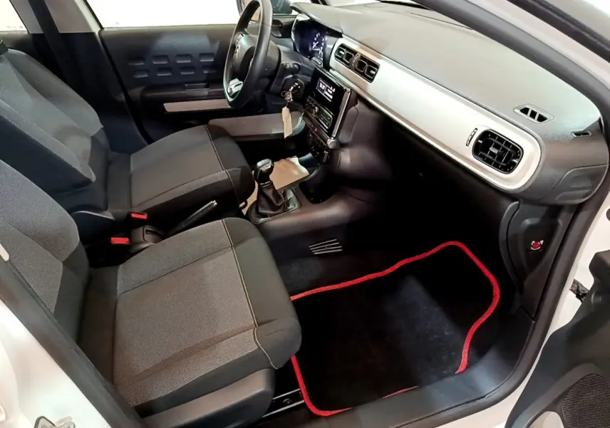 Intérieur avant droit d'une Citroën C3 blanche 2018, sièges gris, tableau de bord clair et tapis noir à bordure rouge.