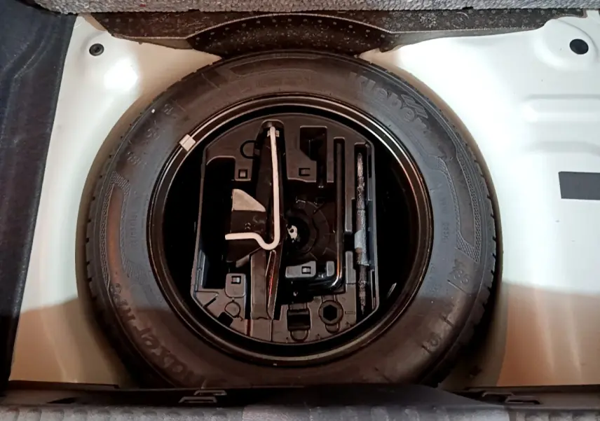 Vue plongeante sur la roue de secours noire et son compartiment blanc dans le coffre d'une Citroën C3 blanche.