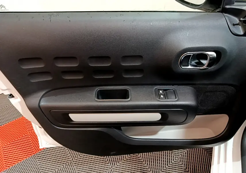 Vue rapprochée de la porte côté gauche d'une Citroën C3 blanche, avec poignée intérieure chromée et commandes de vitres.