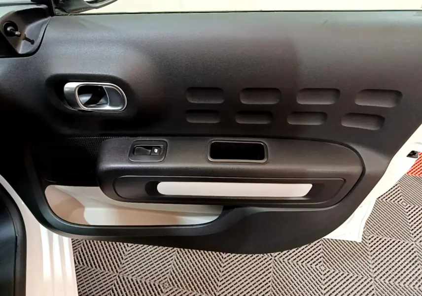Vue rapprochée de la porte côté gauche de la Citroën C3 blanche, mettant en valeur la poignée intérieure et le bouton de lève-vitre.