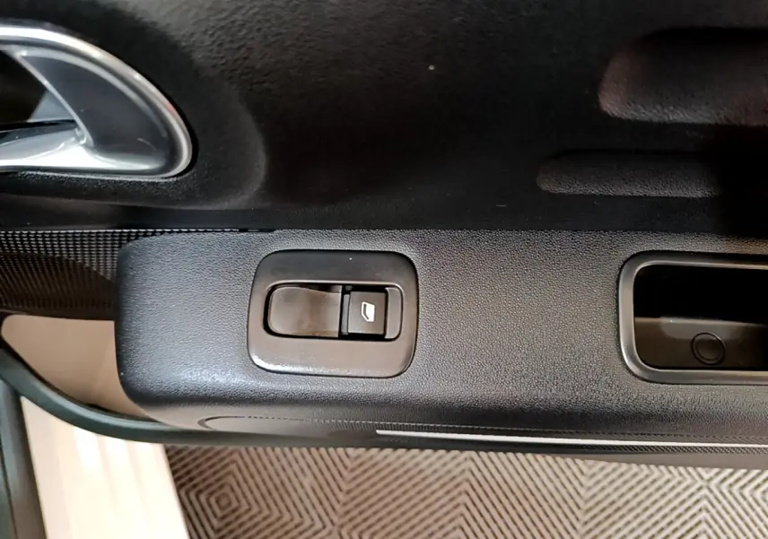 Gros plan sur le bouton de commande de la vitre électrique côté gauche de la porte intérieure noire d'une Citroën C3 blanche.
