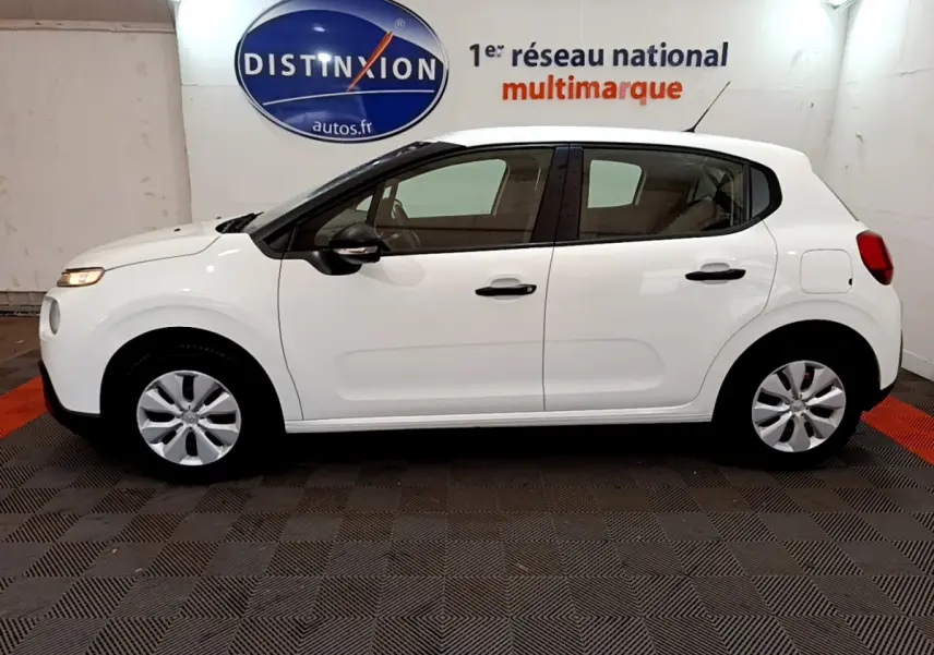 Profil latéral gauche d'une Citroën C3 blanche 2018, avec poignées et rétroviseurs noirs dans un showroom.