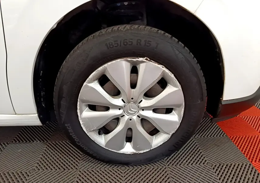 Gros plan sur la roue avant gauche d'une Citroën C3 blanche avec enjoliveur endommagé visible.