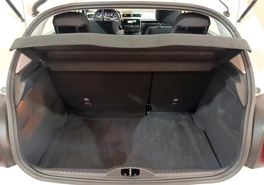 Coffre ouvert vu de l'arrière d'une Citroën C3 blanche avec banquette arrière noire et tablette de coffre relevée.