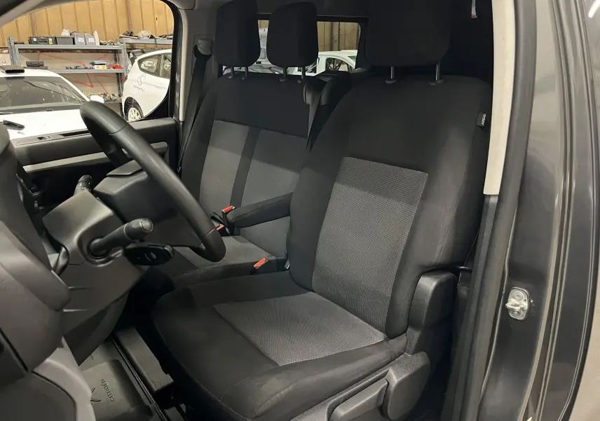 Vue intérieure côté conducteur de l’Opel Vivaro cabine approfondie gris, sièges tissu noir et gris avec accoudoir central.