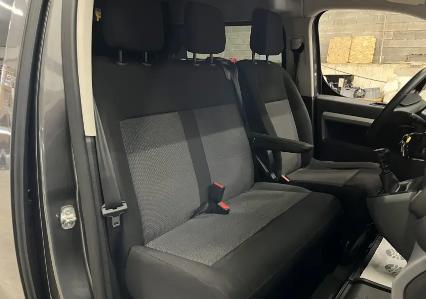 Vue intérieure côté conducteur de l’Opel Vivaro XL gris 2023, montrant les sièges tissu noirs et la boîte manuelle.