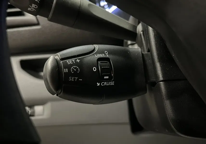 Gros plan sur la commande de régulateur de vitesse noire à gauche du volant dans l'habitacle gris de l'Opel Vivaro XL 2023.