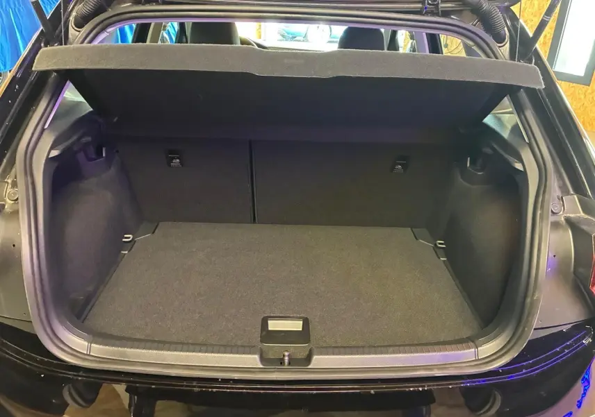 Coffre ouvert vu de l'arrière d'une Volkswagen Polo noire 5 portes, intérieur du coffre tapissé de tissu gris foncé.