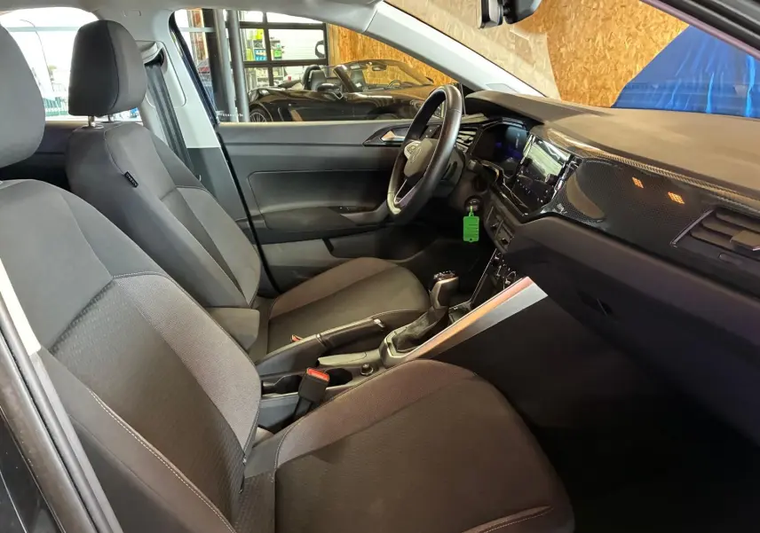 Vue intérieure côté conducteur de la Volkswagen Polo 1.0 TSI noire avec sièges tissu gris et tableau de bord moderne.