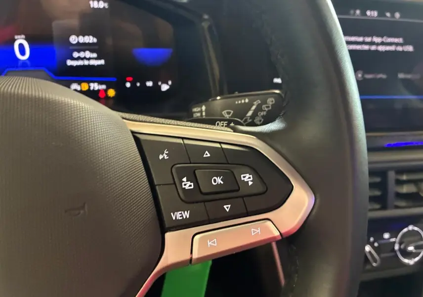 Gros plan sur le volant cuir noir de la Volkswagen Polo 2022, avec commandes multifonctions et tableau de bord numérique bleu.