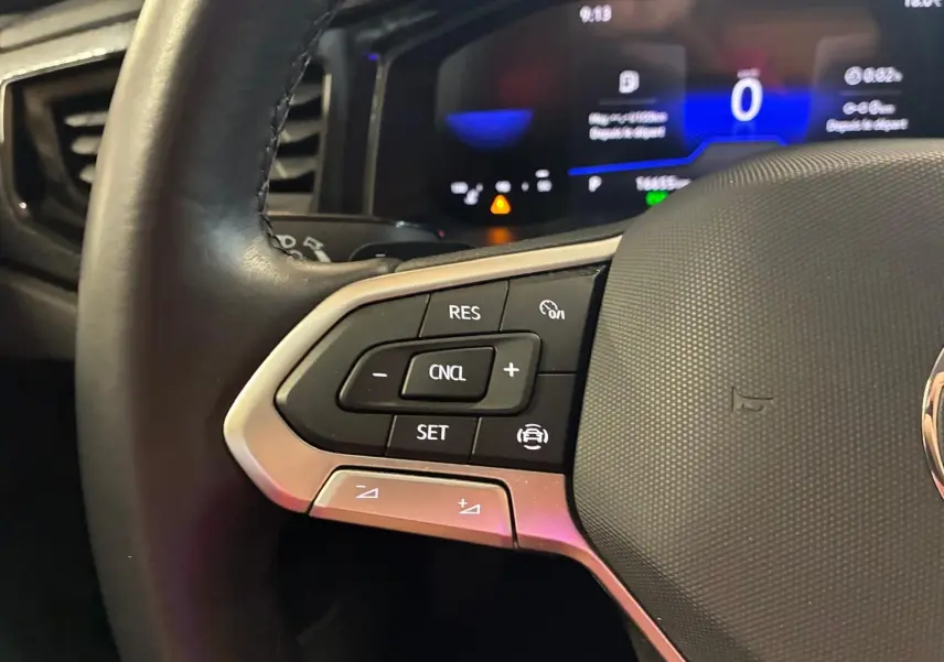 Gros plan sur les commandes du régulateur de vitesse au volant cuir d'une Volkswagen Polo noire, tableau de bord numérique en arrière-plan.