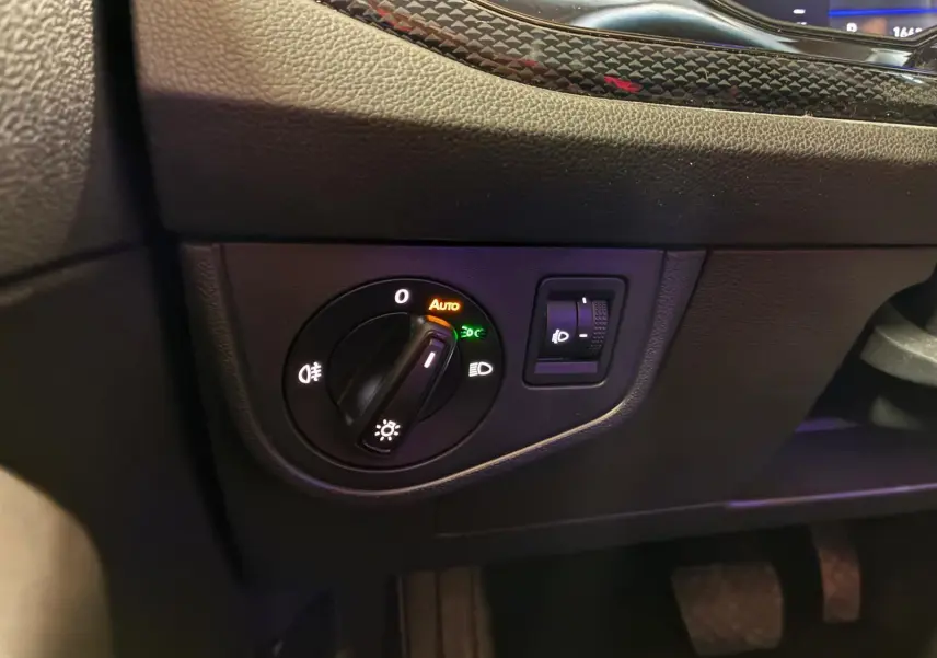 Gros plan sur le bouton de commande des phares avec réglage automatique dans l’habitacle noir de la Volkswagen Polo 2022.