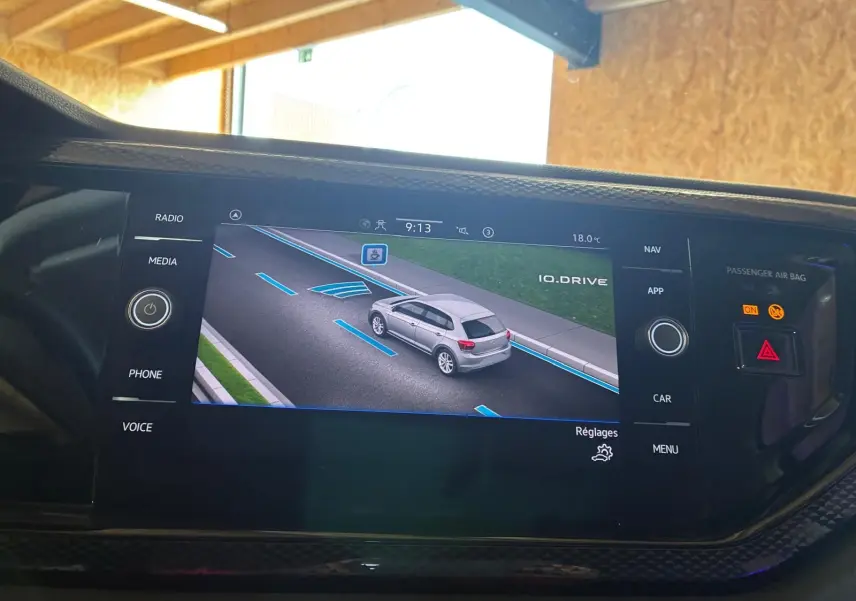 Vue écran intérieur montrant la Polo noire 2022 en 3/4 arrière sur la route avec lignes d'aide au stationnement.
