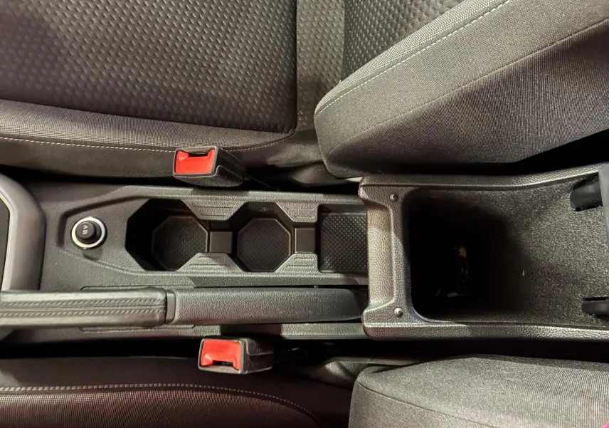 Vue rapprochée de la console centrale noire avec porte-gobelets et frein à main entre les sièges tissu gris foncé du Volkswagen Polo 2022.