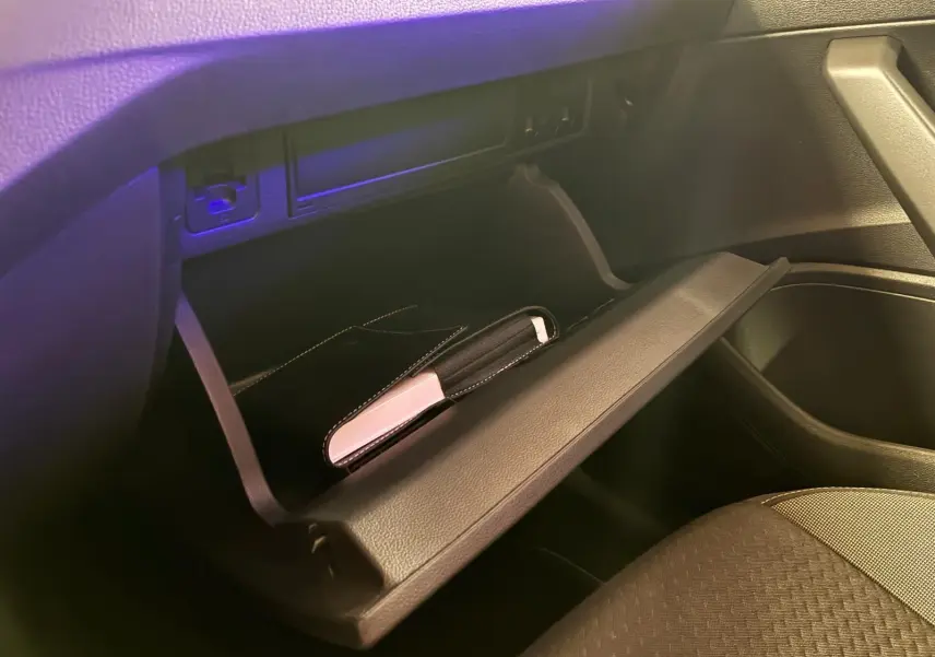 Vue intérieure du coffre à gants ouvert d'une Volkswagen Polo noire, montrant un étui noir et blanc à l'intérieur.