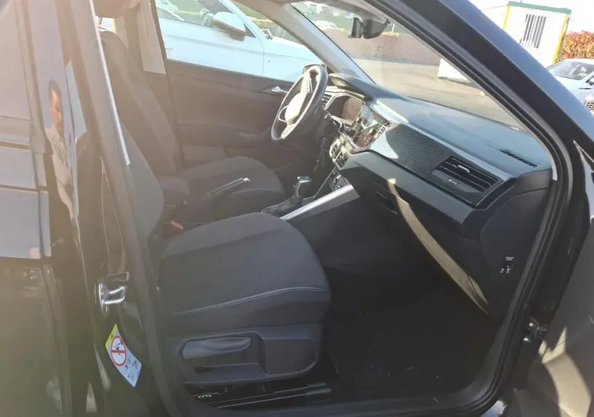 Vue intérieure côté conducteur de la Volkswagen Polo noire 2022, montrant sièges tissu et tableau de bord moderne.