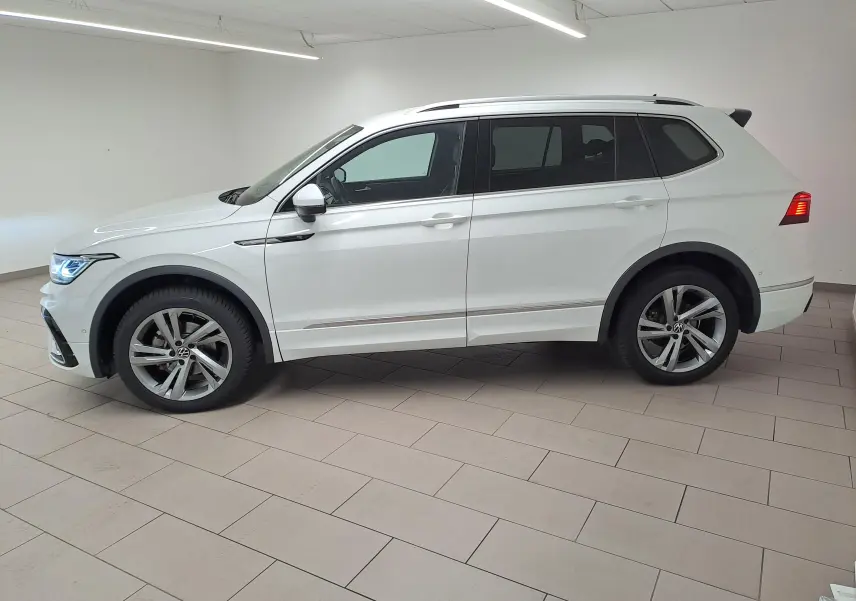 Vue de profil côté gauche du Volkswagen Tiguan Allspace blanc pur 2023 en finition R-Line avec jantes alliage et feux allumés.