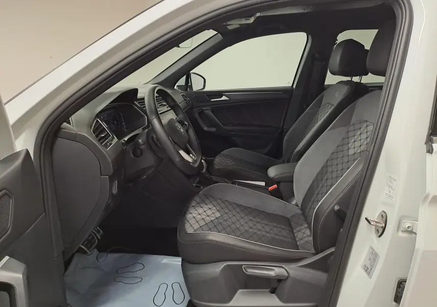Vue intérieure côté conducteur du Volkswagen Tiguan Allspace blanc pur 2023, sièges R-Line en tissu noir à motifs losanges.