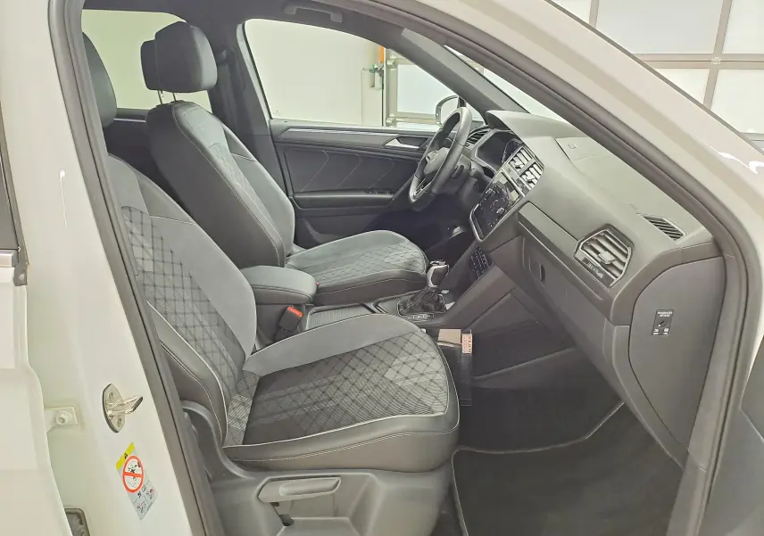 Vue intérieure côté conducteur du Volkswagen Tiguan Allspace blanc pur 2023, sièges en tissu noir à motifs géométriques.