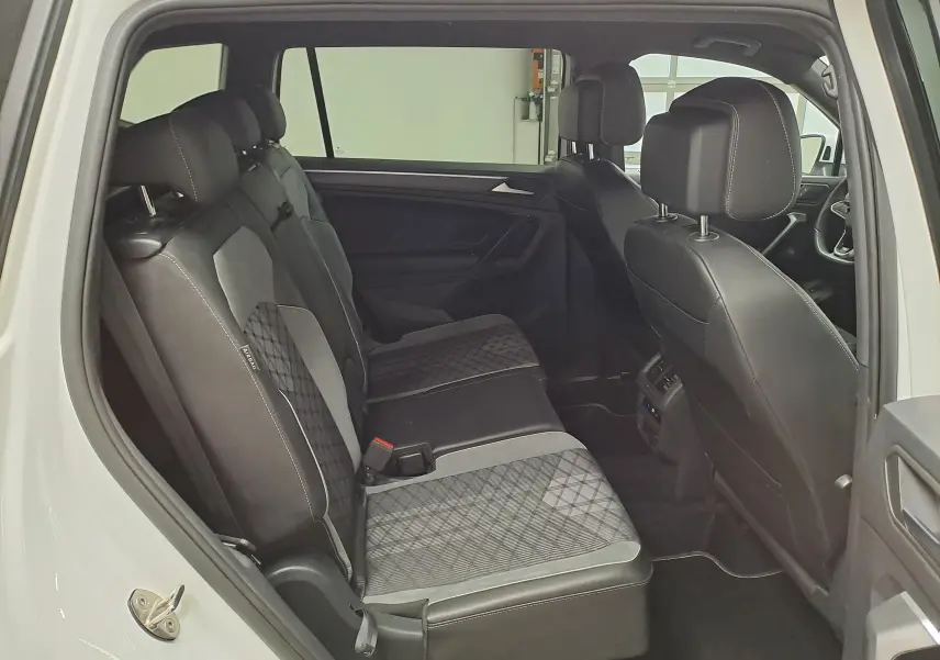 Vue intérieure côté gauche des sièges arrière du Volkswagen Tiguan Allspace blanc pur 2023 avec sellerie tissu et cuir noir.