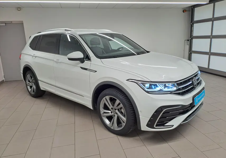 Vue 3/4 avant d'un Volkswagen Tiguan Allspace blanc pur 2023 en finition R-Line avec phares LED allumés.