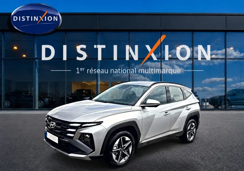 Hyundai Tucson gris shimmering en 3/4 avant droit devant une vitrine Distinxion, jantes alu et lignes anguleuses visibles.