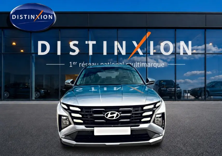 Vue frontale d'un Hyundai Tucson gris shimmering 2026 avec calandre noire distinctive, stationné devant un showroom Distinxion.