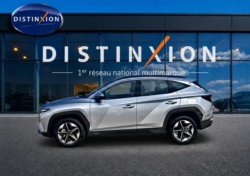 Hyundai Tucson gris shimmering en profil droit devant une vitrine avec logo Distinxion visible en arrière-plan.