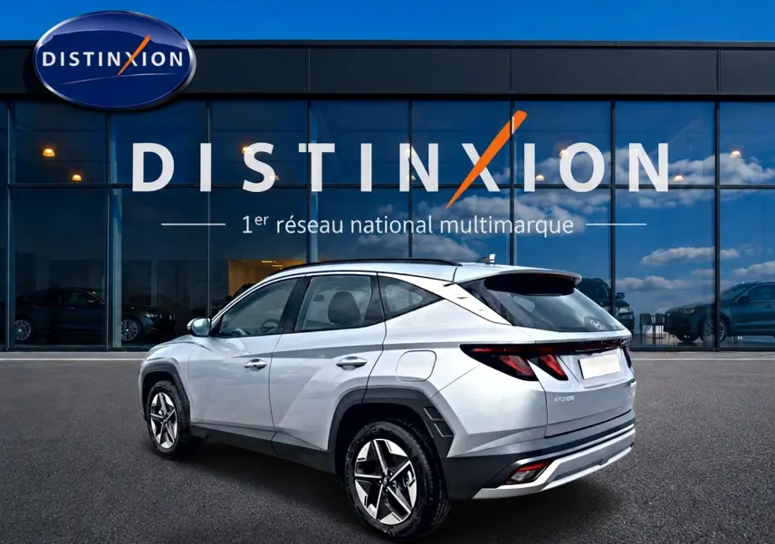 Vue 3/4 arrière droite du Hyundai Tucson gris shimmering devant une vitrine avec logo Distinxion.