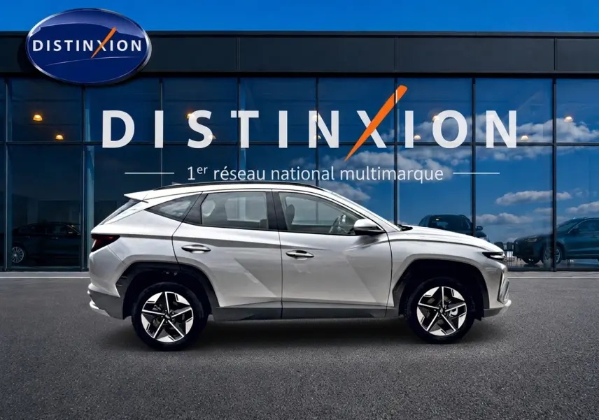 Profil côté gauche du Hyundai Tucson 2026 gris shimmering devant une vitrine avec logo Distinxion.