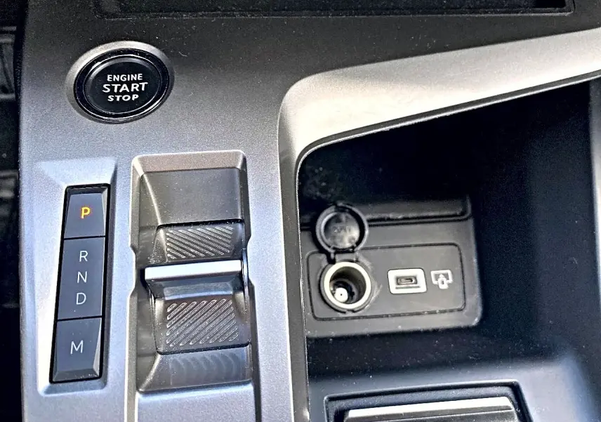 Gros plan sur la console centrale grise de la Peugeot 308 2025 montrant la commande de boîte auto et prise USB avec allume-cigare.