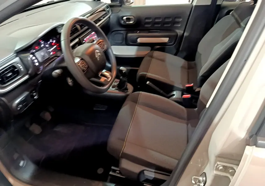 Intérieur de la Citroën C3 beige, vue côté conducteur montrant le tableau de bord et les sièges avant en tissu gris.