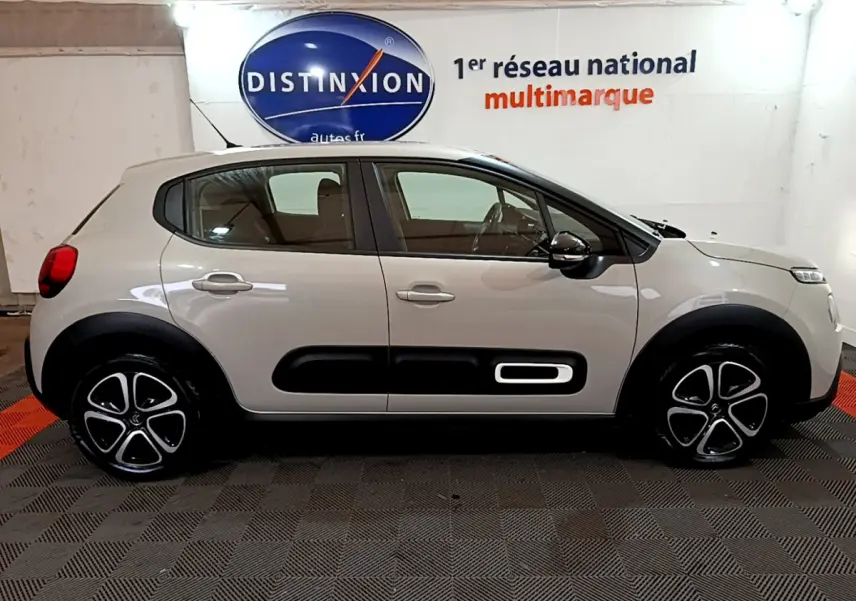 Profil côté gauche d'une Citroën C3 beige 2022 avec protections noires et jantes distinctives en intérieur showroom.
