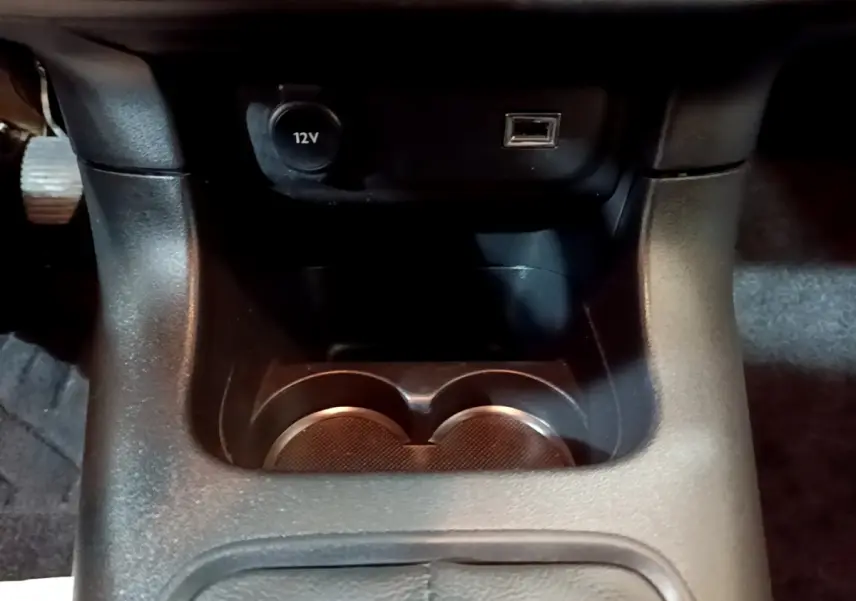 Gros plan sur la console centrale noire de la Citroën C3 beige, montrant prise 12V, port USB et porte-gobelets.