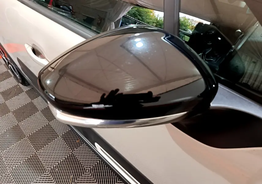 Rétroviseur noir brillant côté gauche de la Citroën C3 beige vue en gros plan sur fond intérieur.