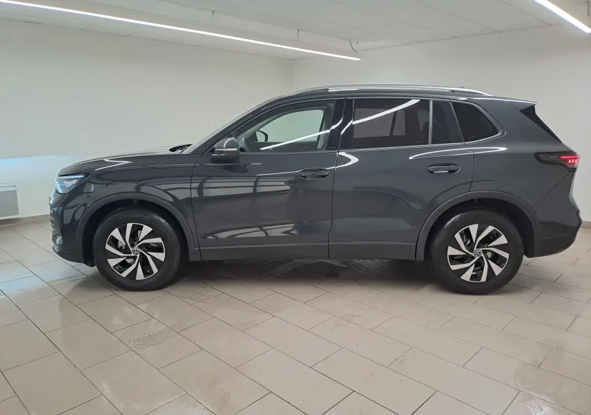Vue de profil côté gauche du Volkswagen Tiguan 2024 gris Urano avec jantes distinctives et attelage escamotable visible.