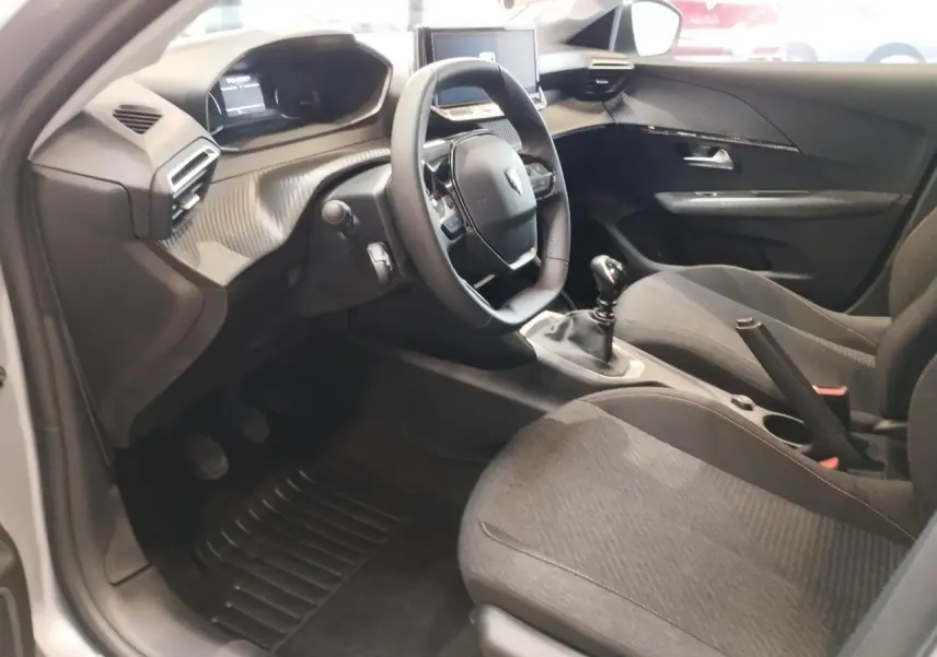 Intérieur avant droit de la Peugeot 208 2025 gris clair, volant cuir, boîte manuelle et tableau de bord moderne.